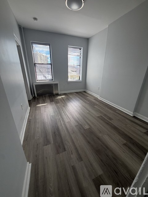 A room with wooden flooring and two windows.