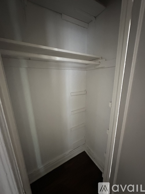 A small, empty, white closet with a wooden floor.