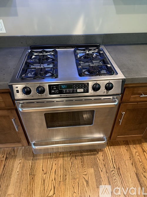 A stainless steel gas stove with a digital display and control panel is installed in a kitchen with wooden cabinets.