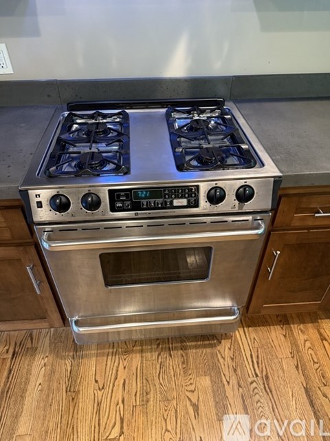 A stainless steel gas stove with a digital display and control panel is installed in a kitchen with wooden cabinets.