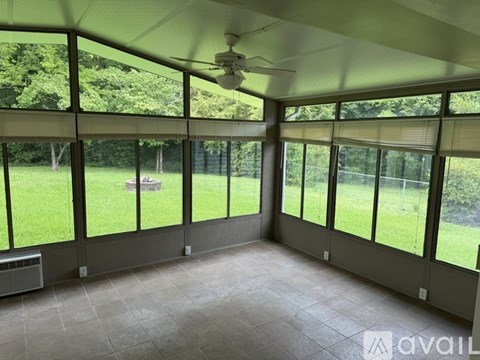 A room with a ceiling fan and large windows overlooking a grassy area.