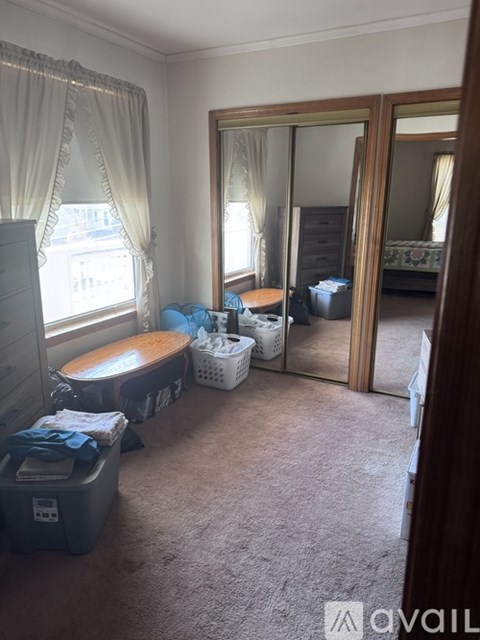 A bedroom with a large mirror and a window with curtains.