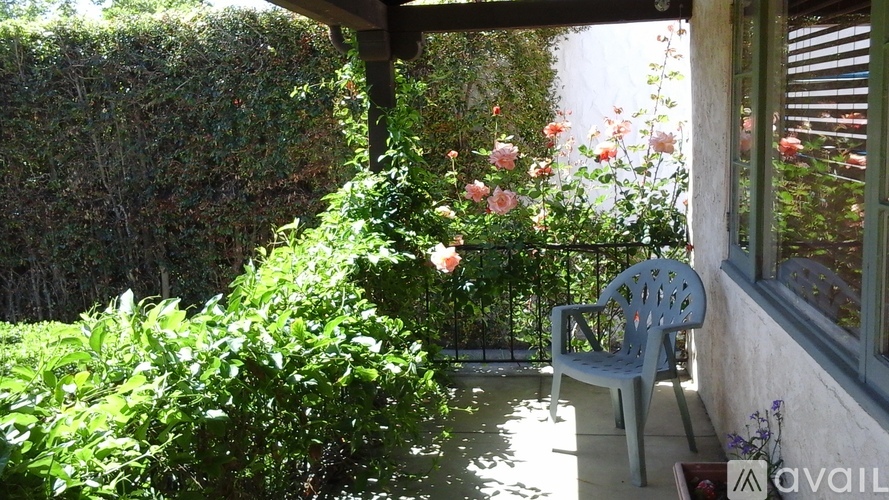 A grey chair is on a patio with a hedge and flowers behind it.