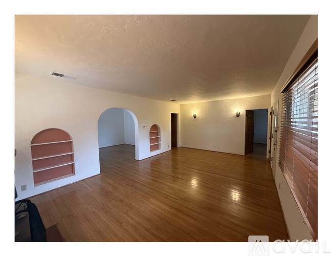 A room with wooden floors and white walls with a window on the right side.