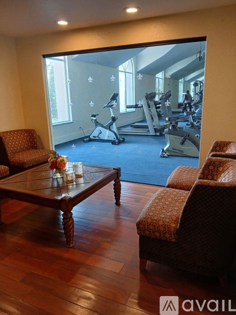 A living room with a coffee table and chairs in front of a mirror showing a gym.