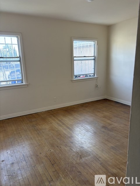 A room with wooden flooring and two windows.