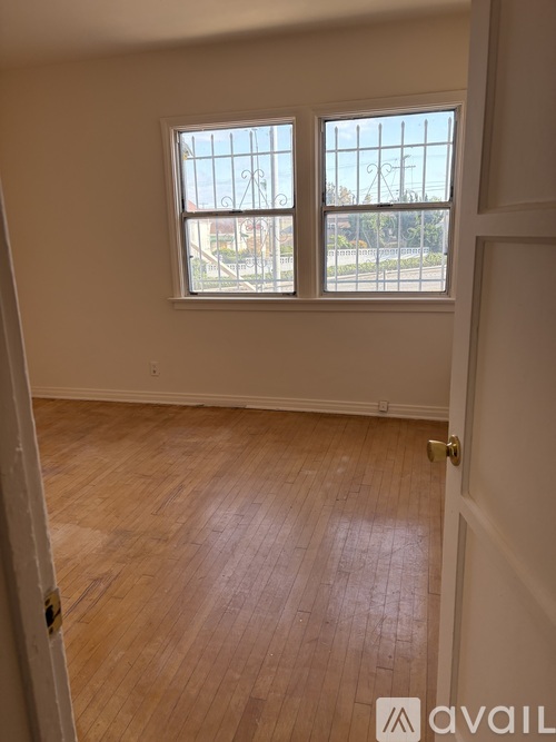 A room with wooden flooring and two windows.
