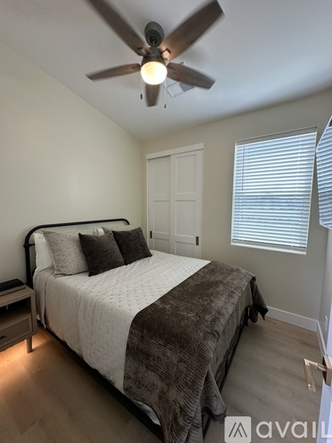 A bedroom with a bed, nightstand, and window with blinds.