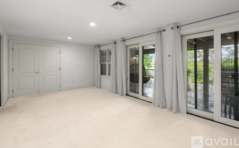 A spacious room with white walls and a large window with curtains.