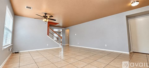 A spacious room with a fan and a staircase.