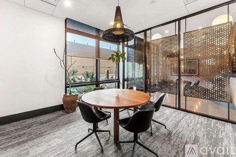 A conference room with a round table and chairs, a hanging light fixture, and a view of the outdoors through a glass wall.