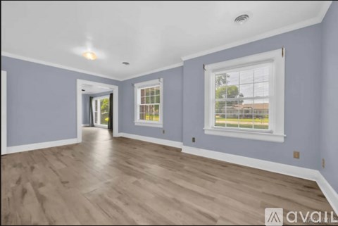 A spacious room with light wood flooring and two windows.