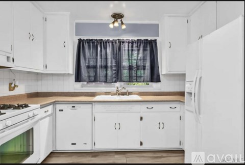 A kitchen with white cabinets and a window with curtains.