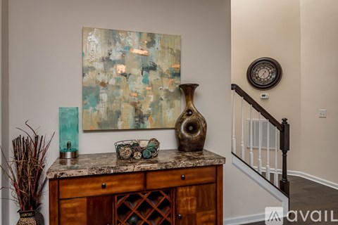 A large abstract painting hangs on a wall above a wooden cabinet with a vase on top.