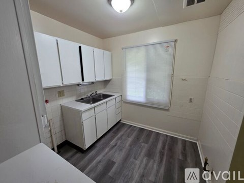 A kitchen with white cabinets and a window with blinds.