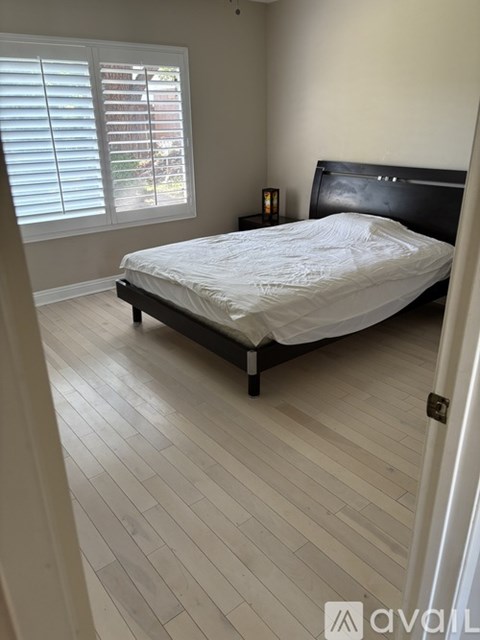 A bedroom with a bed, wooden floors, and a window with blinds.