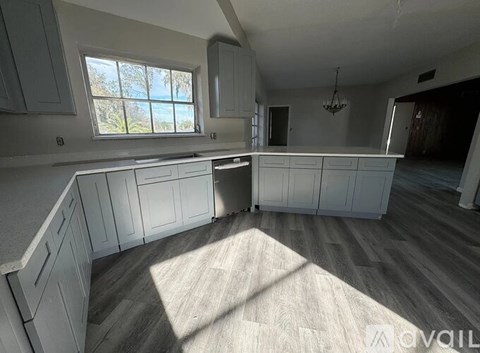 A spacious kitchen with white cabinets and a large window.