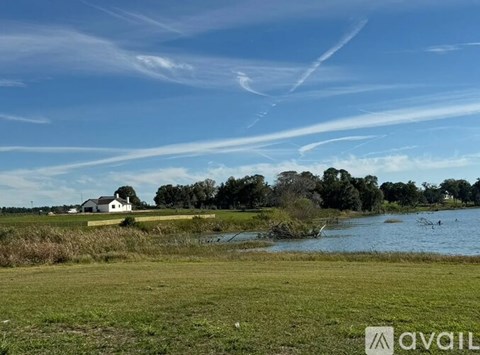 A house is situated by a body of water with a grassy field in the foreground.