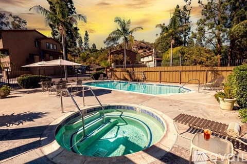 A hot tub sits in the middle of a patio with a pool and a house in the background.