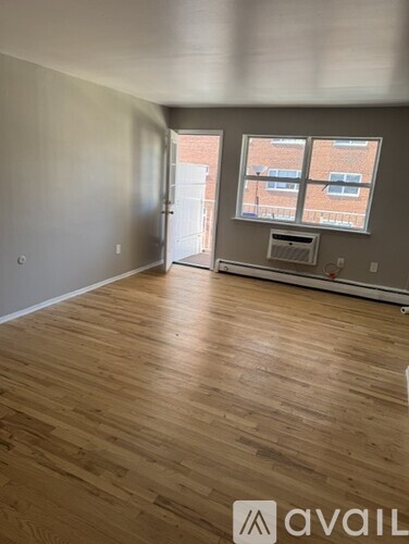 A room with wooden flooring and a window overlooking a brick building.
