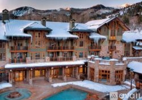 A large, luxurious house with a pool in the foreground and snow-covered mountains in the background.