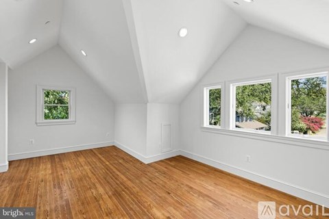 A room with wooden floors and white walls, with windows showing a view of trees and a house.