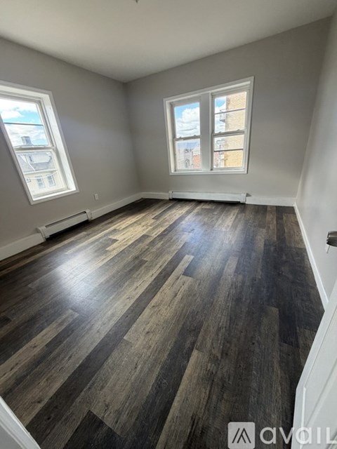 A room with wooden flooring and two windows.