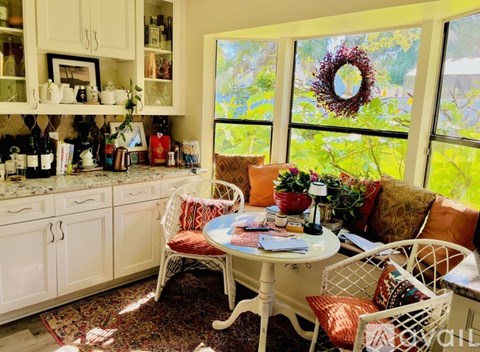 A white table with a red pillow and a wreath on the window.