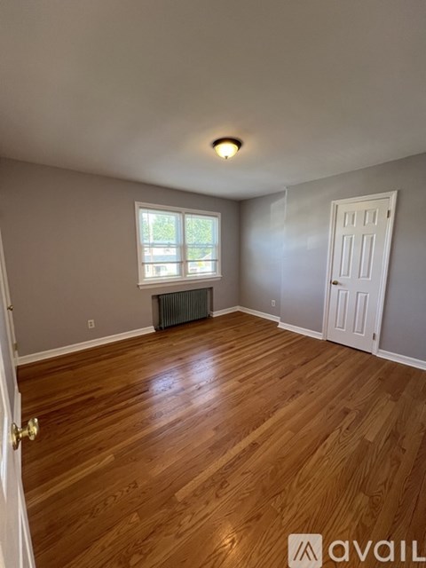 A room with wooden flooring and a window with a view of trees.