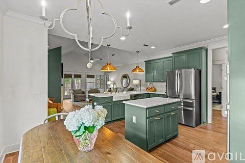 A kitchen with green cabinets and a wooden table with a vase of flowers on it.