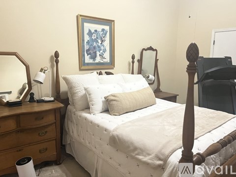 A bedroom with a white bed and a wooden dresser.