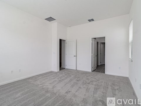 A spacious room with carpeted floor and white walls, featuring a doorway leading to another room.