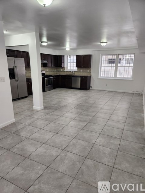 A spacious kitchen and living room with tile flooring and white walls.