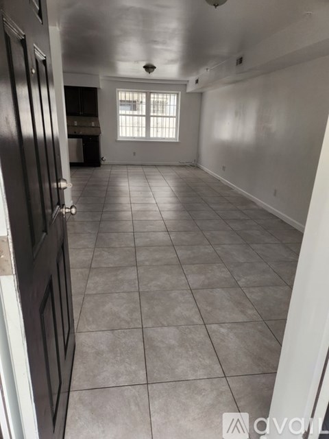 A room with white walls and tile flooring, with a door on the left and a window on the right.