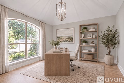 A room with a desk, chair, and a large window with a view of trees.