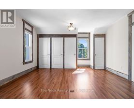 A room with wood floors and white walls, with a window showing trees outside.