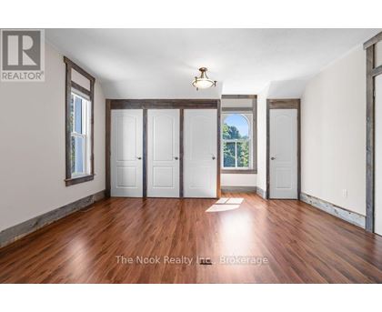 A room with wood floors and white walls, with a window showing trees outside.