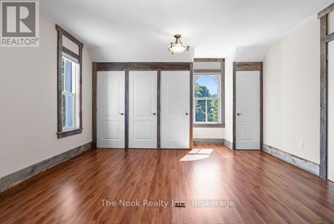 A room with wood floors and white walls, with a window showing trees outside.
