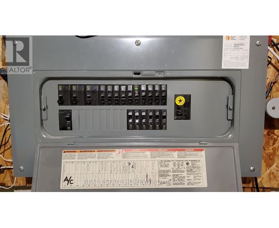 A grey electrical panel with a yellow warning label and a Real Estate Home Warranty sticker.