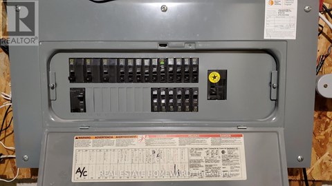 A grey electrical panel with a yellow warning label and a Real Estate Home Warranty sticker.