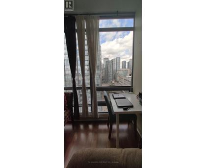 A room with a desk and chair in front of a window with a view of a city skyline.