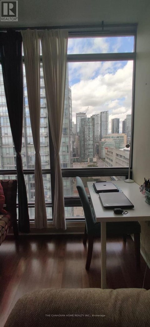 A room with a desk and chair in front of a window with a view of a city skyline.