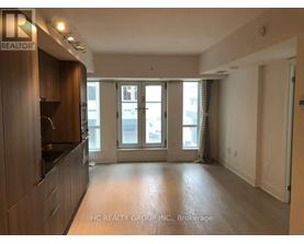 A spacious living room with a kitchen area to the left and a sliding glass door leading to a balcony.