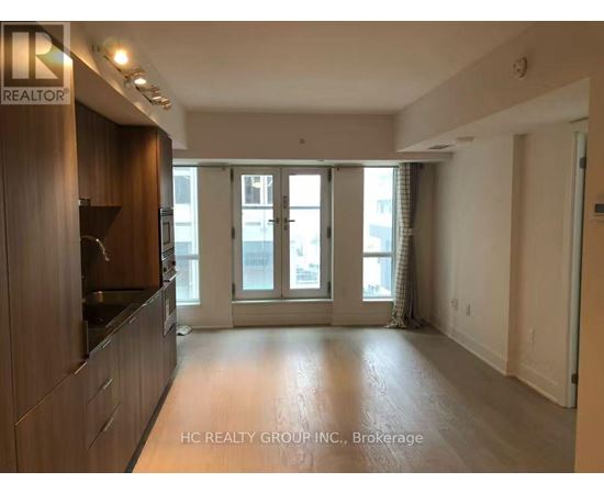 A spacious living room with a kitchen area to the left and a sliding glass door leading to a balcony.