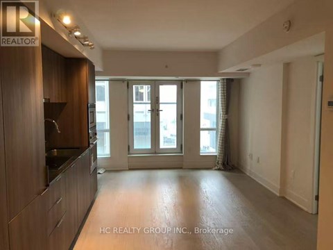 A spacious living room with a kitchen area to the left and a sliding glass door leading to a balcony.