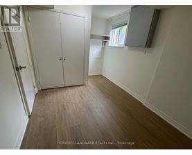 A room with a wooden floor and white walls, with a door on the left and a window on the right.