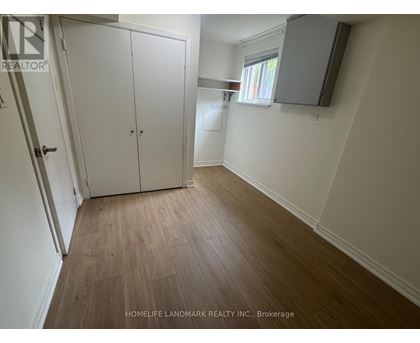 A room with a wooden floor and white walls, with a door on the left and a window on the right.