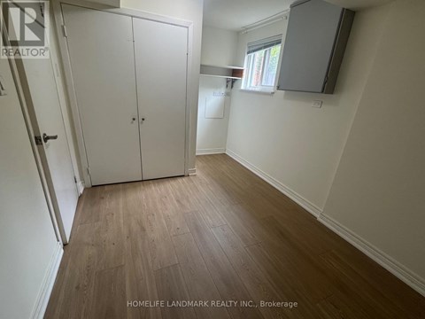 A room with a wooden floor and white walls, with a door on the left and a window on the right.