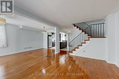 A spacious room with wooden floors and a staircase with black railings.
