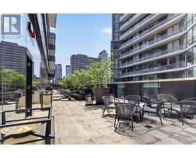 A patio with chairs and tables is in front of a tall building.